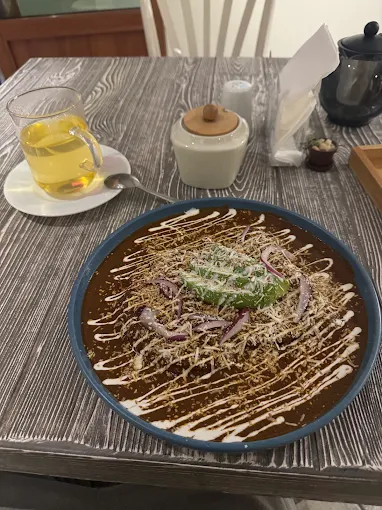 Plato de mole poblano con crema, queso, aguacate y té